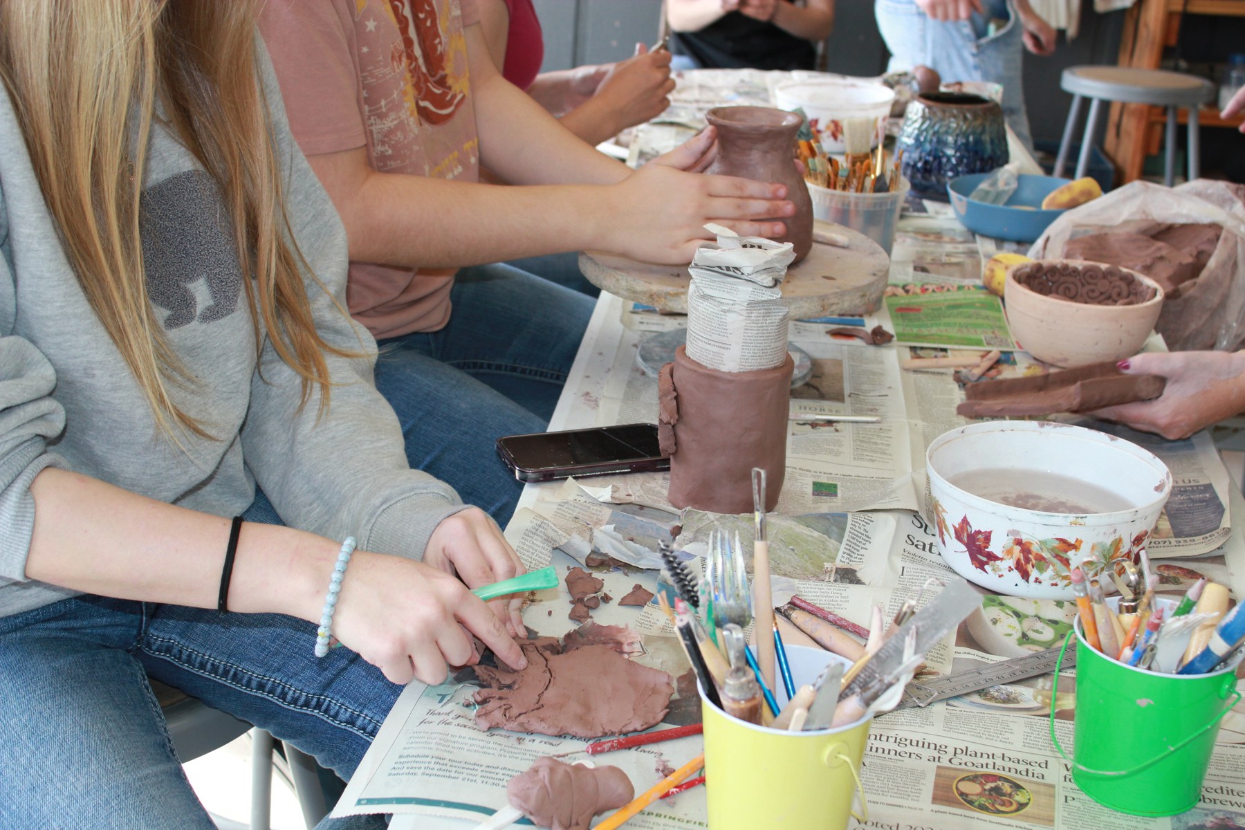 Students shaping clay vessels at an outdoor table